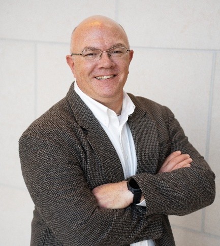 Andy smiling wearing glasses and a brown jacket
